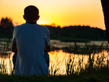 Boynuna kulaklık takmış bir adam gölün kıyısındaki güzel yaz günbatımını seyrediyor.