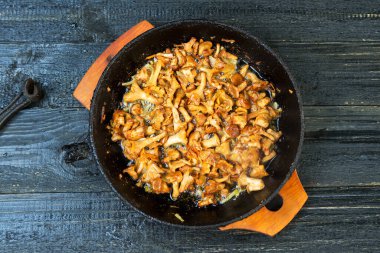 Kırsal siyah ahşap bir masada, dökme demir bir tavada kızarmış mantarlar.