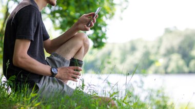 Bir yaz günü parkta dinlenen telefonu ve kahvesi olan genç beyaz bir adam.