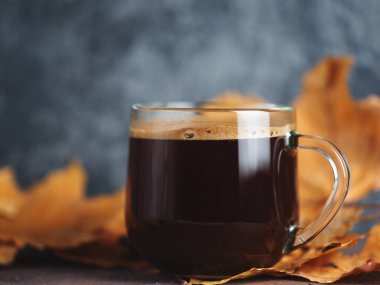 Arka planda sonbahar kuru yaprakları olan cam espresso kahve fincanı. Sıcak kahveyle soğuk mevsim