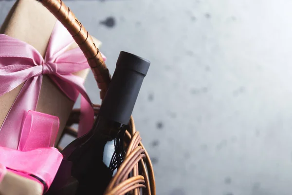 A bottle of red wine and a gift box with a bow in a basket with copyspace