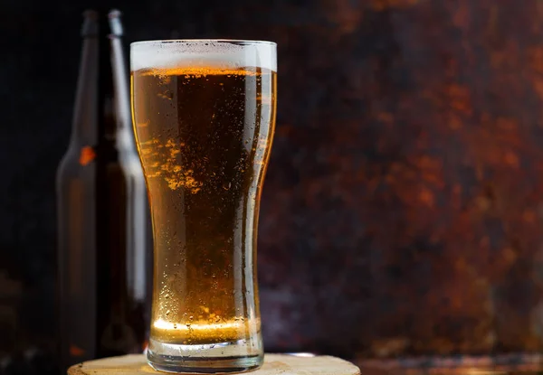 A glass of cold light beer on a dark rusty metal background copy space