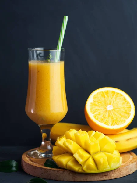 Yellow smoothie with mango, banana and orange in a glass. Delicious fast and healthy food