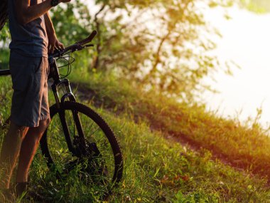 Cyclist next to the bike in the green summer forest at sunset close-up
