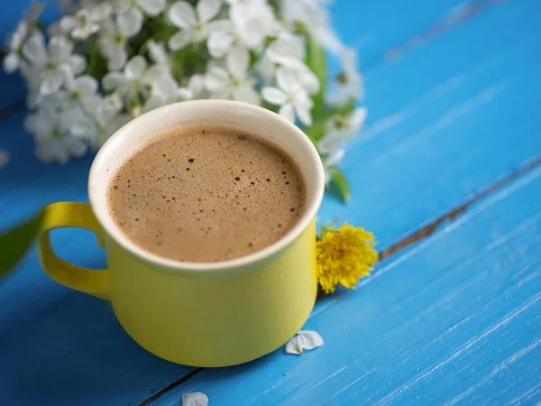 Spring coffee . Yellow Cup on blue background and cherry blossoms