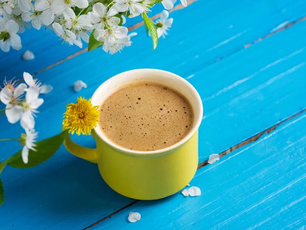 Spring coffee . Yellow Cup on blue background and cherry blossoms