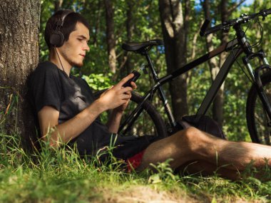 Ağacın yanındaki parkta dinlenen bisikletçi. Yazın parkta bisiklet sürerim. Etkin yaşam biçimi