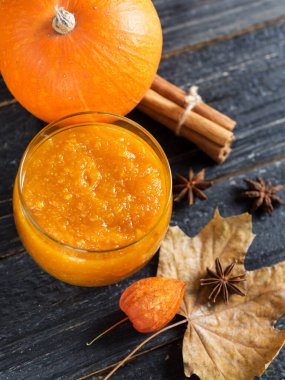 Sonbahar yaprakları ve tarçın çubuklarıyla ahşap bir zeminde kavanozda kabak reçeli.