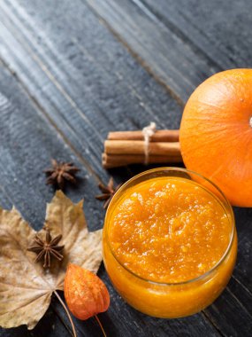 Sonbahar yaprakları ve tarçın çubuklarıyla ahşap bir zeminde kavanozda kabak reçeli.