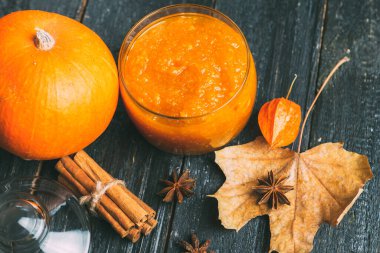 Sonbahar yaprakları ve tarçın çubuklarıyla ahşap bir zeminde kavanozda kabak reçeli.