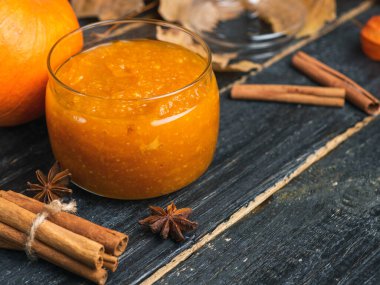 Sonbahar yaprakları ve tarçın çubuklarıyla ahşap bir zeminde kavanozda kabak reçeli.