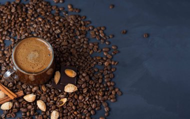 Beton bir masada rendelenmiş bademle birlikte bir bardak kahve ve dağınık kavrulmuş tahıllar.