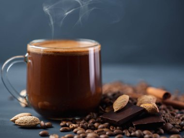 Beton bir masada rendelenmiş bademle birlikte bir bardak kahve ve dağınık kavrulmuş tahıllar.