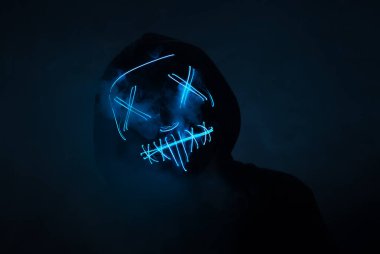 Korkunç neon parlayan maskeli bir adam ve karanlık bir arka planda dumanlı bir başlık. Korku ve Cadılar Bayramı konsepti