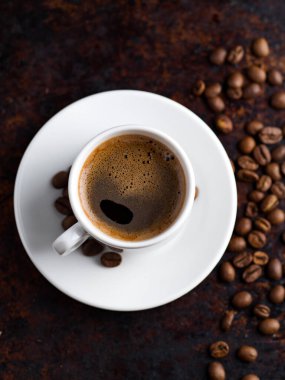 Beyaz espresso kahve fincanı, paslı arka planda, dağınık kahve çekirdekleri.