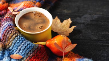 Sarı espresso fincanı ahşap masanın üzerinde sonbahar yaprakları, balkabağı ve renkli bir sonbahar eşarbı. Sıcaklık ve rahatlık. Boşluğu kopyala