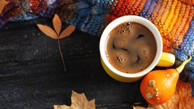 Sarı espresso fincanı ahşap masanın üzerinde sonbahar yaprakları, balkabağı ve renkli bir sonbahar eşarbı. Sıcaklık ve rahatlık. Boşluğu kopyala