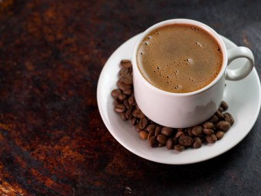 Beyaz espresso kahve fincanı, paslı demir kahverengi arkaplan ve kahve çekirdekleri.