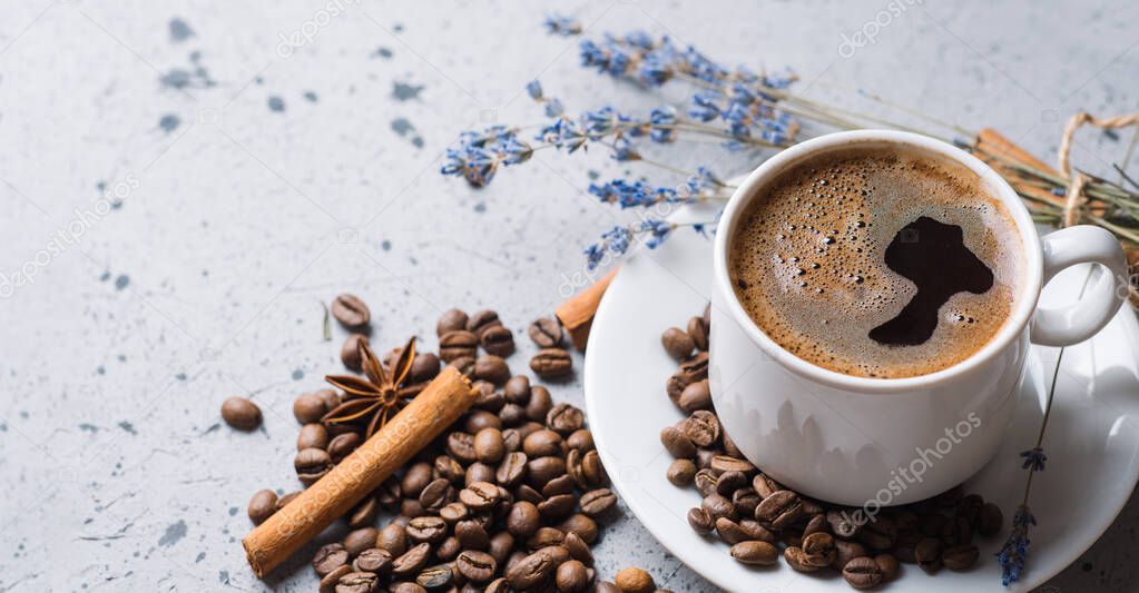 A cup of aromatic espresso coffee on a white table, a stick of cinnamon, anise, scattered roasted coffee beans, copy space banner