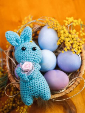 Pençelerinde bir çiçekle örülmüş Paskalya tavşanı, sepette renkli pastel yumurtalar.