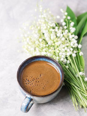 Beyaz beton bir masada bir fincan sade kahve ve bir buket bahar çiçeği vadi çiçekleri.
