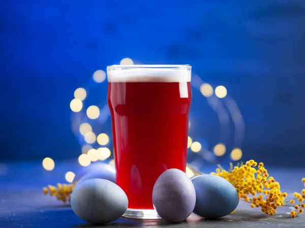 Bayramlık Paskalya masasında bir bardak kırmızı bira boyalı yumurta ve mimoza dallarıyla birlikte.