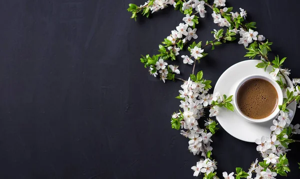 A Cup of coffee on a concrete table with branches of spring cherry blossoms and copy space