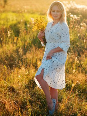 Beyaz elbiseli, sarı çiçekli güzel sarışın. Yazın gün batımında portre