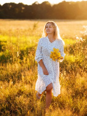 Beyaz elbiseli, sarı çiçekli güzel sarışın. Yazın gün batımında portre