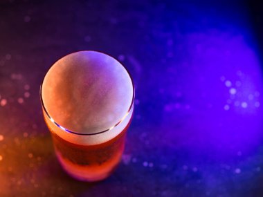 Koyu arkaplanda bir bardak light bira, renkli trend ışığı.