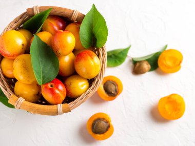 Olgun kayısılar hasır bir tahta sepetin içinde beyaz bir taş masanın üzerinde.