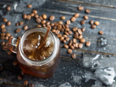 Koyu ahşap bir masanın üzerinde cam bir kavanoz buzlu kahve.