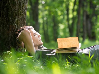 Parkta elinde kitapla çimlerin üzerinde uyuyan sevimli beyaz bir adam. Yaz sabahı parkta bir kitap oku.