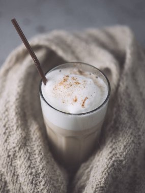 Bir bardak sonbahar kahvesi örgü örülmüş bir eşarba sarılmış gri bir masada.