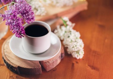 Tahta bir masanın üzerinde beyaz bir fincan kahve. Beyaz leylak dalları, eski kitaplar.