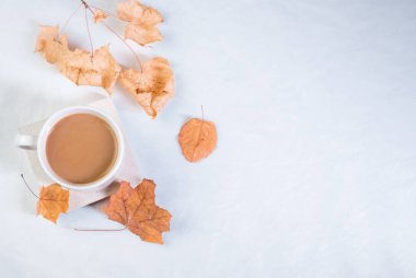 Sütlü bir fincan kahve ve beyaz bir masada kurumuş akçaağaç yaprakları.