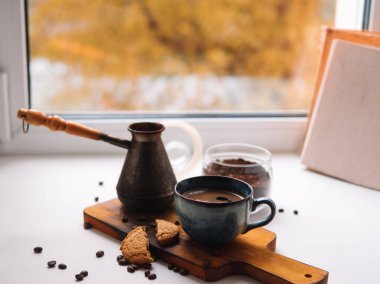 Sonbahar, pencere eşiğinde sakin bir hayattır. Sonbaharda öğleden sonraları ev sıcaklığı ve konfor kavramı. Dzhezva 'dan sıcak kahve, kitap, pencereden manzara.