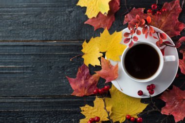 Sarı ve kırmızı akçaağaç yaprakları ve böğürtlen dallarıyla ahşap bir masada beyaz bir espresso fincanı.