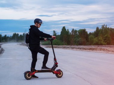 Kask takan genç bir adam bitmemiş bir yolda güçlü, modern bir elektrikli scooter sürüyor. Elektrik taşımacılığı