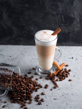 Masanın üzerinde büyük bir bardakta sütlü kahve. Kavrulmuş kahve çekirdekleri, tarçın çubukları.