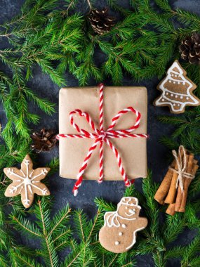 Noel ağacı dalları ve zencefilli kurabiyelerle dolu beyaz ve kırmızı kurdeleli bir hediye kutusu.