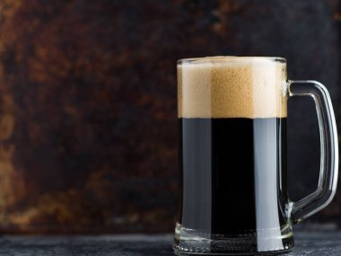 Paslı arka planda köpük kapaklı bir bardak koyu bira.