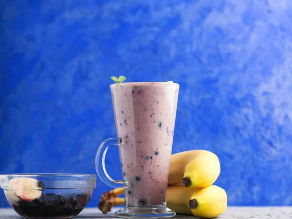 Kubek Szklany Jagodami Koktajlem Bananowym Niebieskim Tle — Zdjęcie stockowe