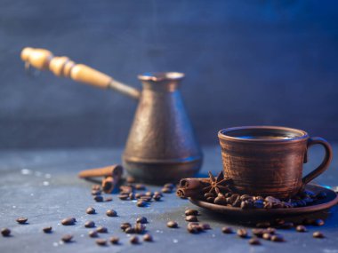 Kil kahve fincanı, ahşap saplı bakır jezva kavrulmuş kahve çekirdekleri, tarçın çubuğu ve anason. koyu arkaplan renkli mavi ışıkla aydınlatılmış