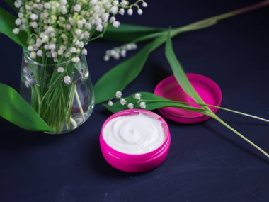 Cilt veya yüz için krem, koyu taş bir masanın üzerinde, bir buket bahar çiçeği vadideki zambakların çiçekleri