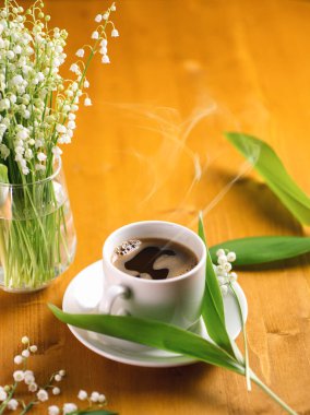 Bahar kahvaltısı, ahşap bir masada beyaz bir fincan espresso kahve, vadide bir buket bahar zambağı.