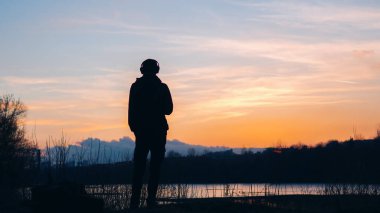 Yalnız bir adam renkli bir bahar günbatımına bakar. Özgürlük ve seyahat aşkı kavramı. Doğada kulaklıkla müzik dinlemek.
