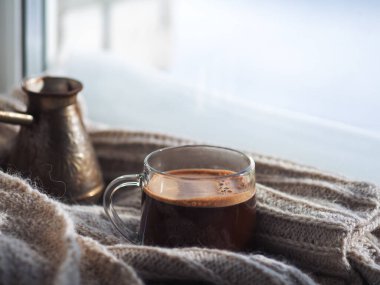 Bir bardak sıcak espresso kahvesi, Türk dzhezve 'inde demlenmiş, pencerenin dışında kış.