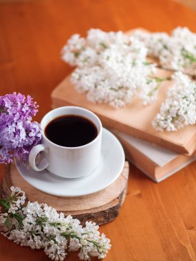 Bahar havası, ahşap bir masada bir fincan aromatik espresso kahve, çiçek açan leylak dalları ve bir kitap.