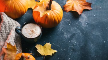 Sütlü ve tarçınlı bir fincan sonbahar kahvesi. Akçaağaç yaprağı ve olgun dekoratif balkabaklarıyla örülmüş sıcak bir eşarp.